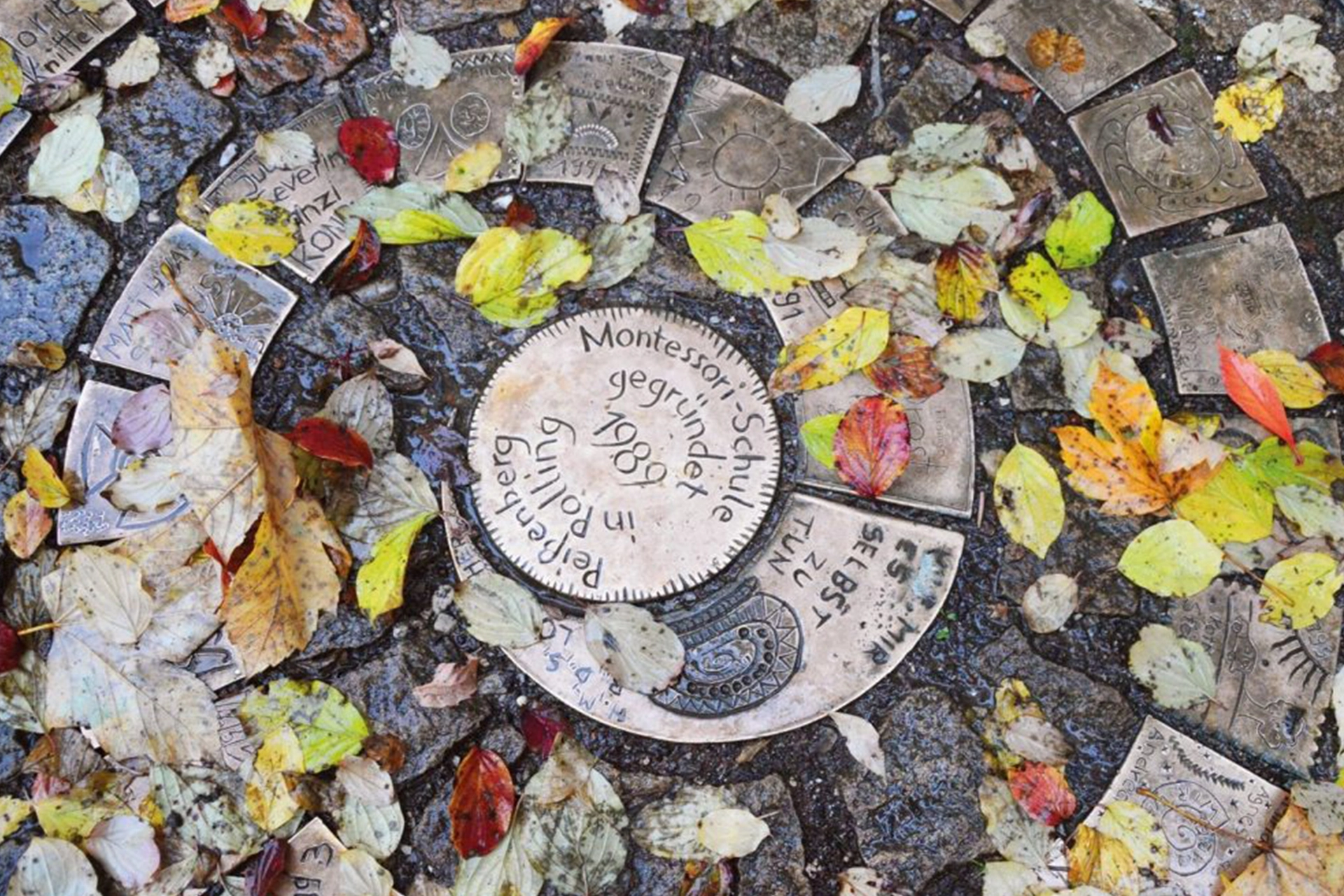 Bronzespirale im Garten der Montessori Schule Peißenberg bedeckt mit buntem Herbstlaub